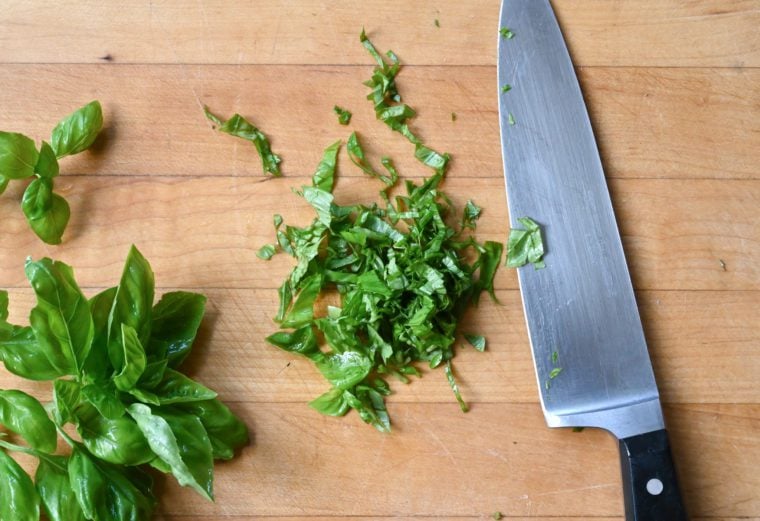 Chopped herbs on a cutting board with a chef\'s knife.