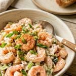 Shrimp salad in white bowl on wooden table with toast in background.