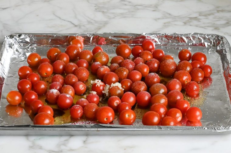 tomatoes, oil, vinegar, garlic and seasoning on baking sheet