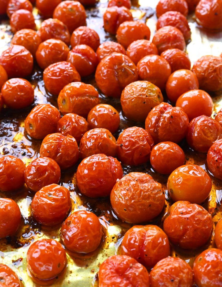 Roasted cherry tomatoes on a lined baking sheet.