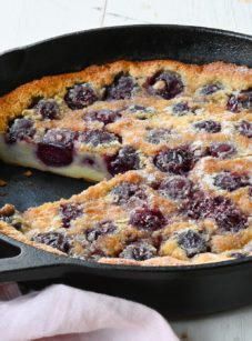 Partially sliced cherry clafoutis in a skillet.