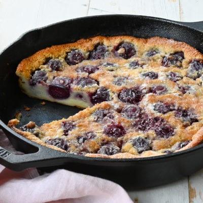 Partially sliced cherry clafoutis in a skillet.