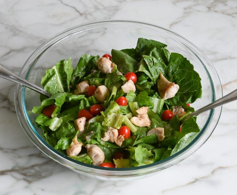tossing the greens, chicken, and tomatoes with the dressing