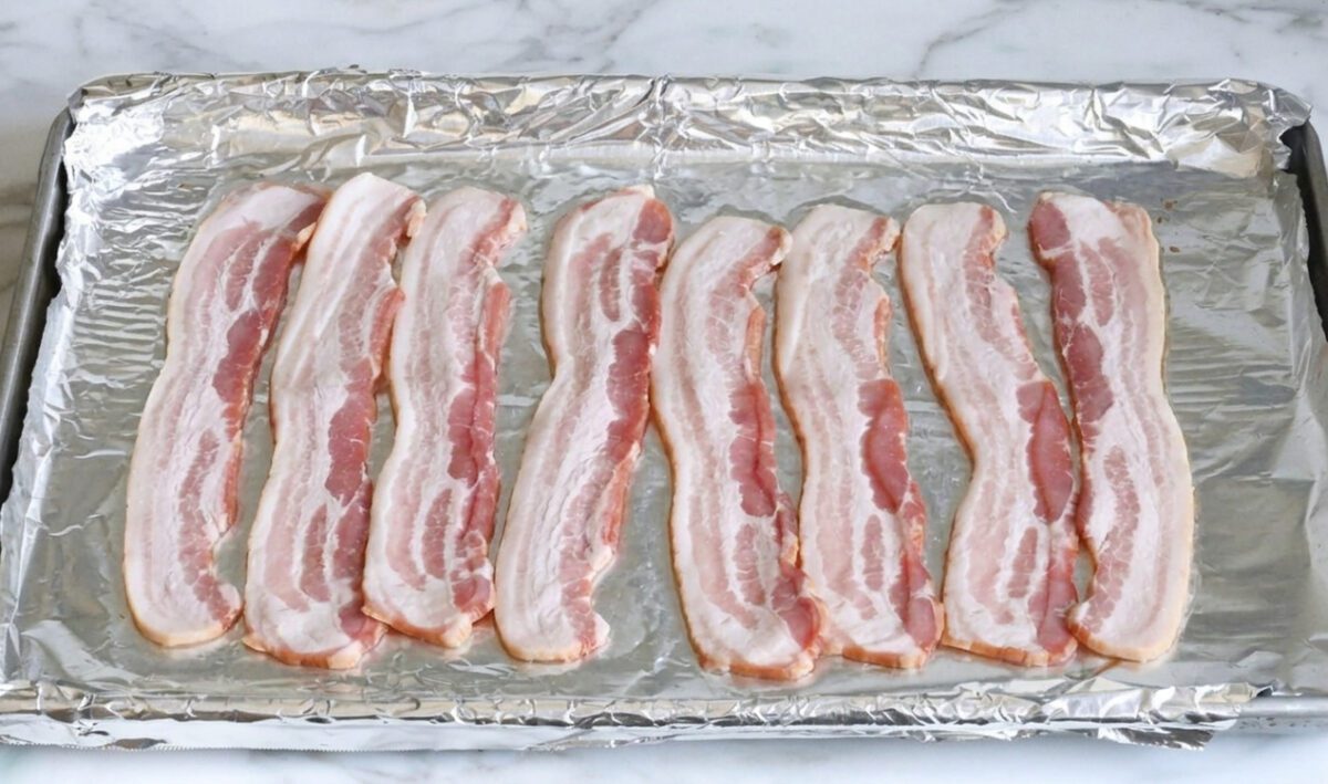 Raw strips bacon on foil-lined sheet pan.