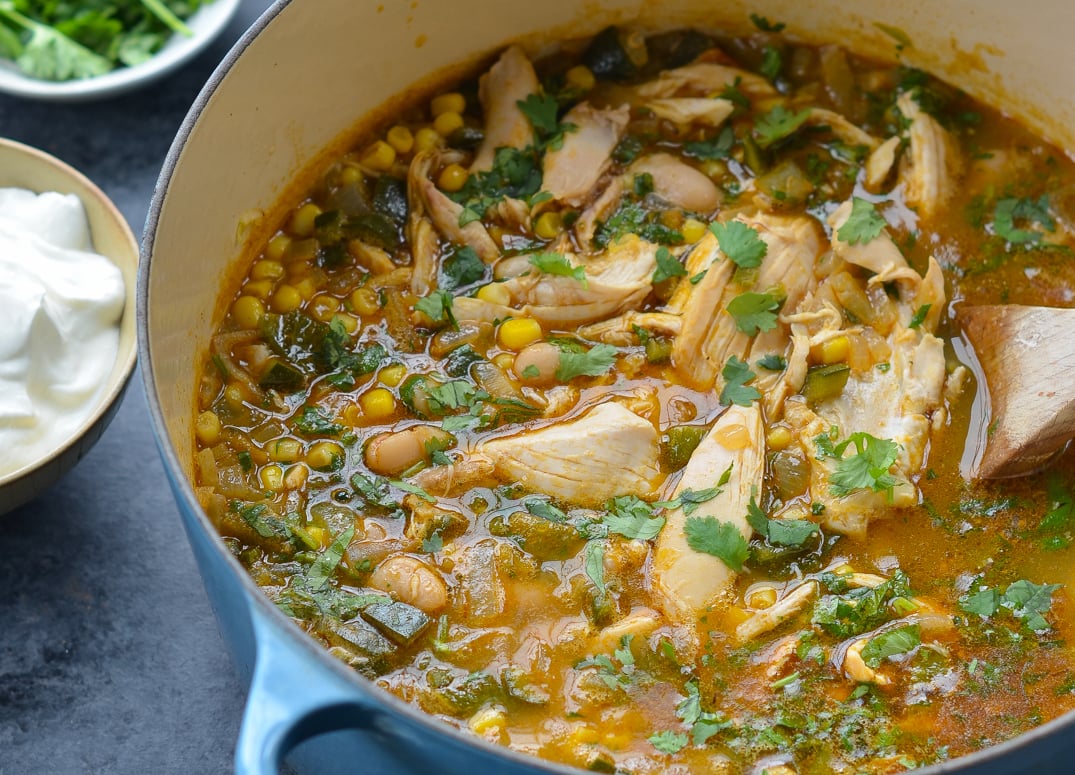 white chicken chili in dutch oven with bowl of sour cream on side. 