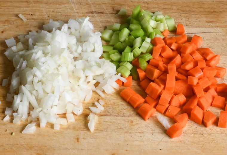Chopped onion, celery, and carrot on a wooden cutting board.