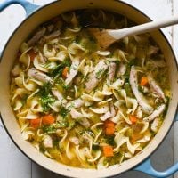 Chicken noodle soup in a Dutch oven with a wooden spoon.
