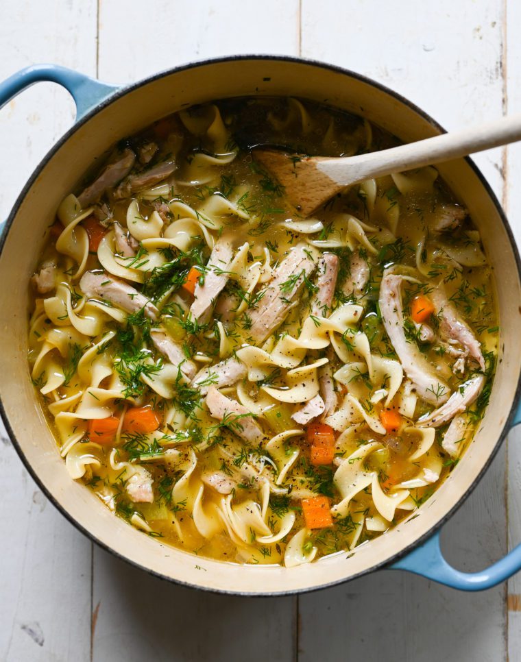 Chicken noodle soup in a Dutch oven with a wooden spoon.