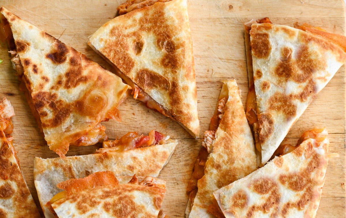 chicken quesadillas on wooden cutting board with limes and sour cream