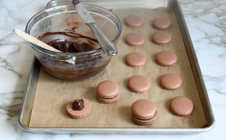 adding chocolate ganache to chocolate macaron shells