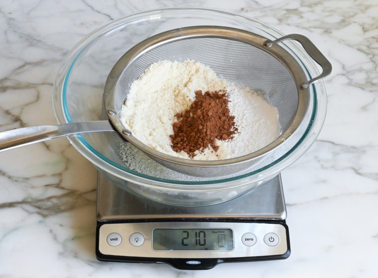 weighing and sifting almond flour with confectioners sugar and cocoa powder