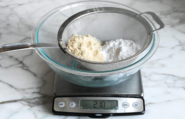 weighing almond flour and confectioners sugar in a fine sieve over a bowl