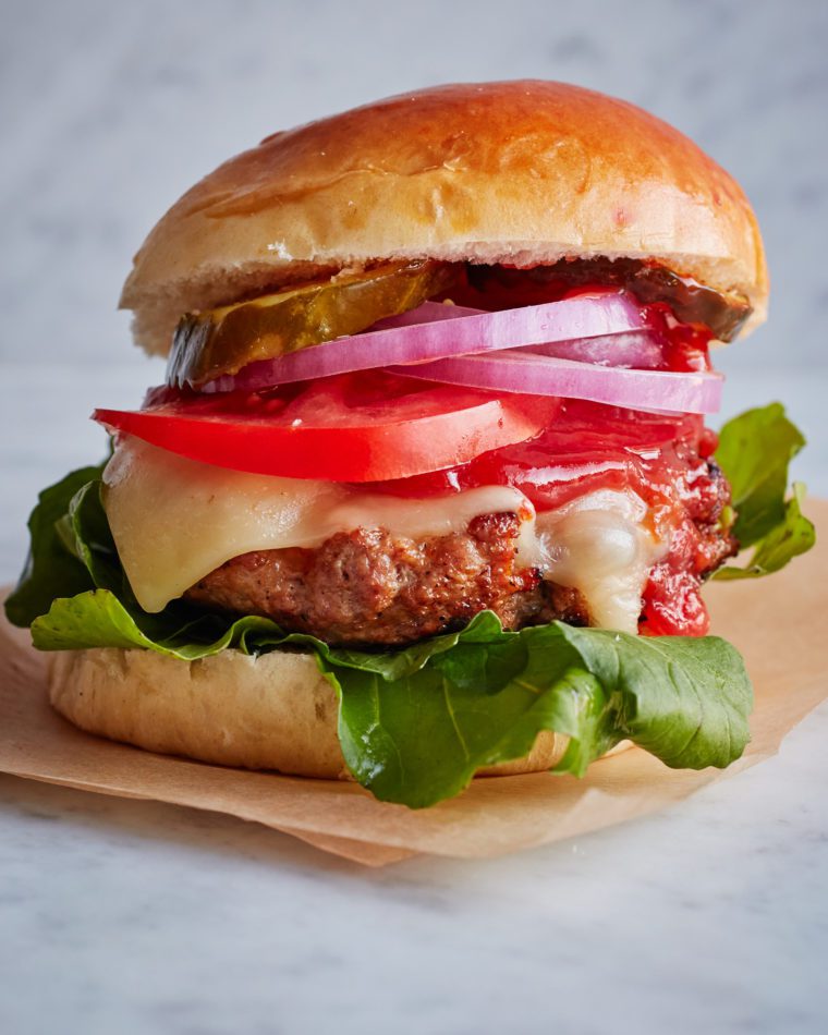 Burger piled with toppings on parchment paper.