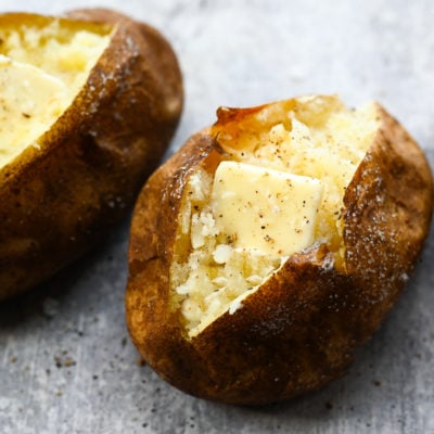 Two baked potatoes with butter on parchment paper.