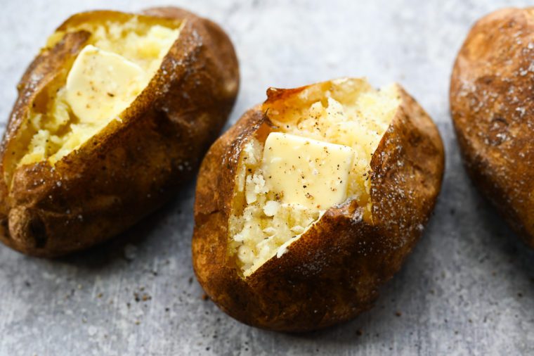 Two baked potatoes with butter on parchment paper.