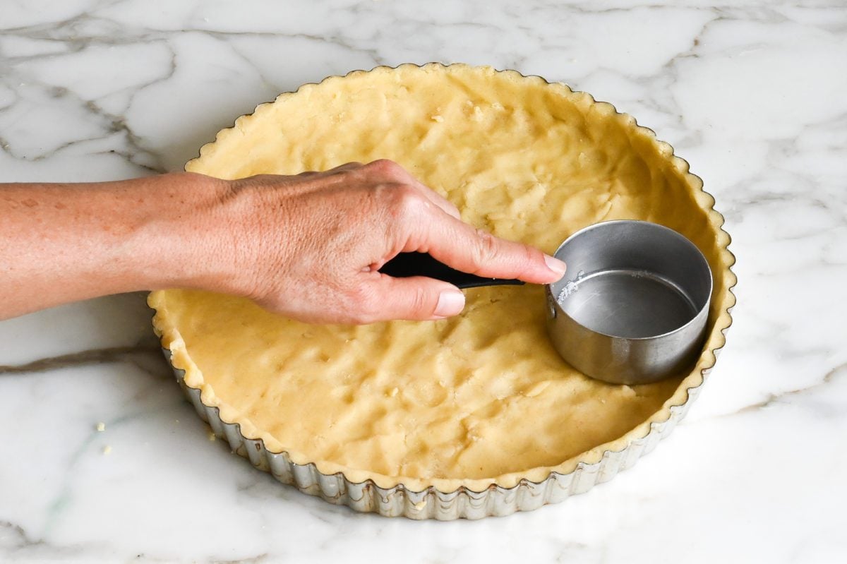 Using a measuring cup to even out edges of tart crust dough.