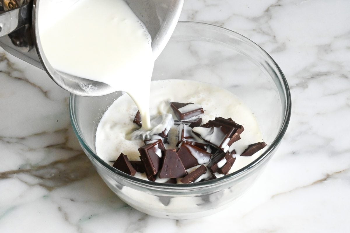 Pouring hot cream into bowl of chopped chocolate.