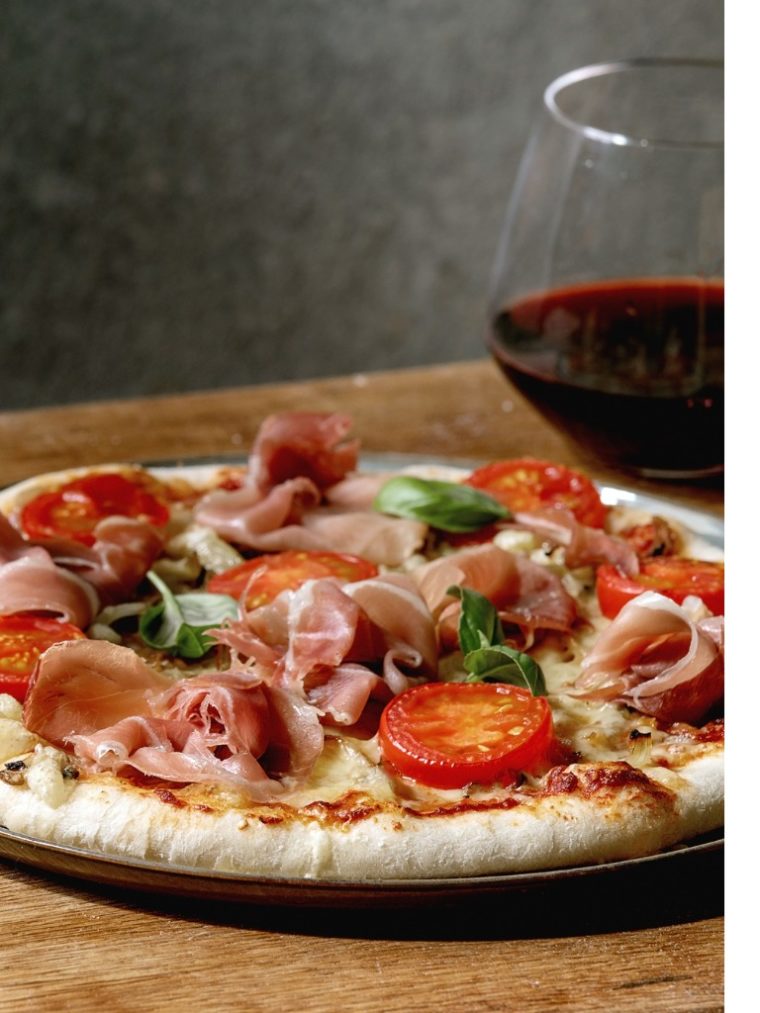 Glass of red wine with a pizza.
