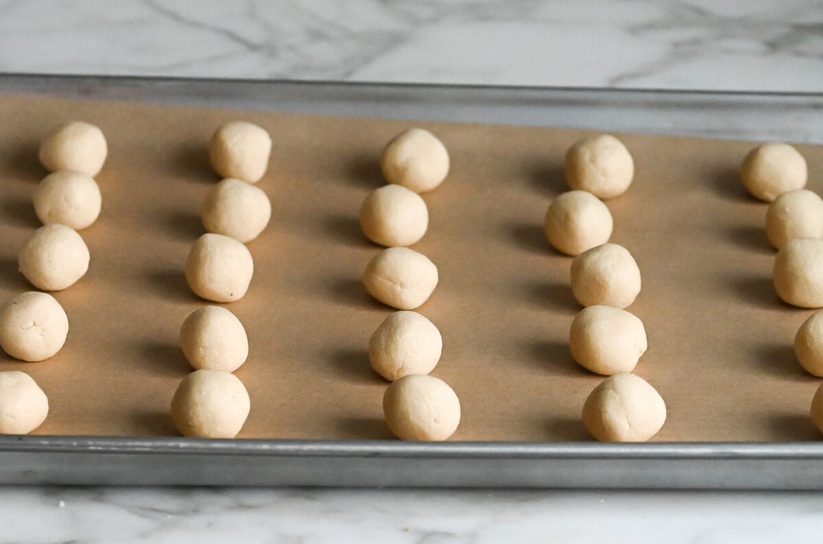 snowball cookie dough balls on parchment-lined baking sheet