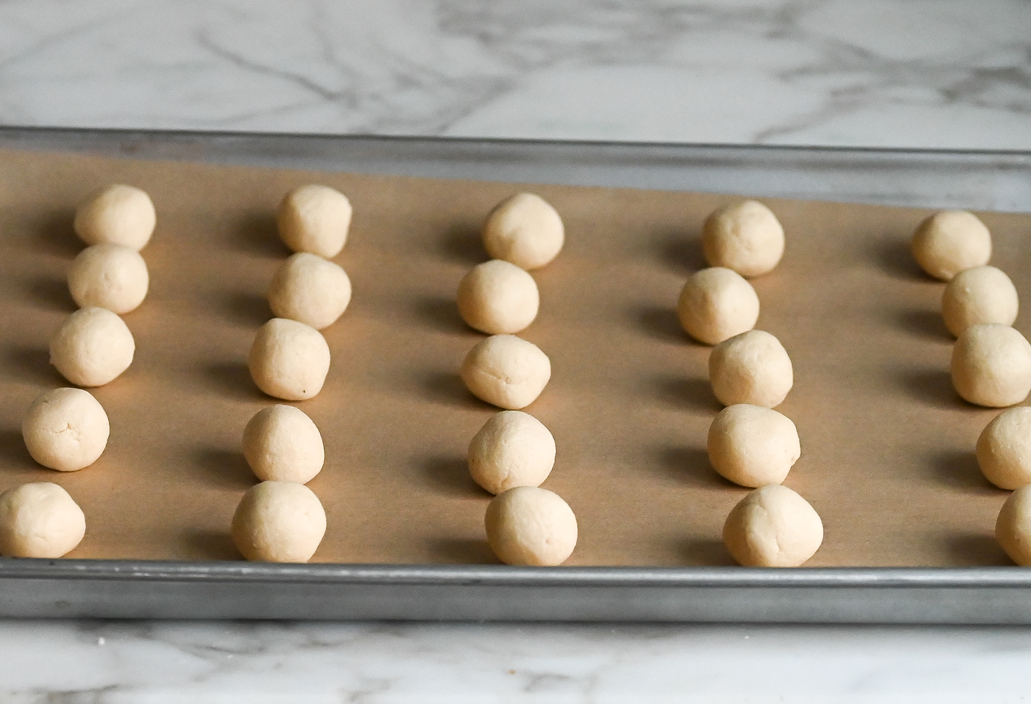 snowball cookie dough balls on parchment-lined baking sheet