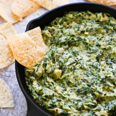 Tortilla chip in a bowl of spinach artichoke dip.