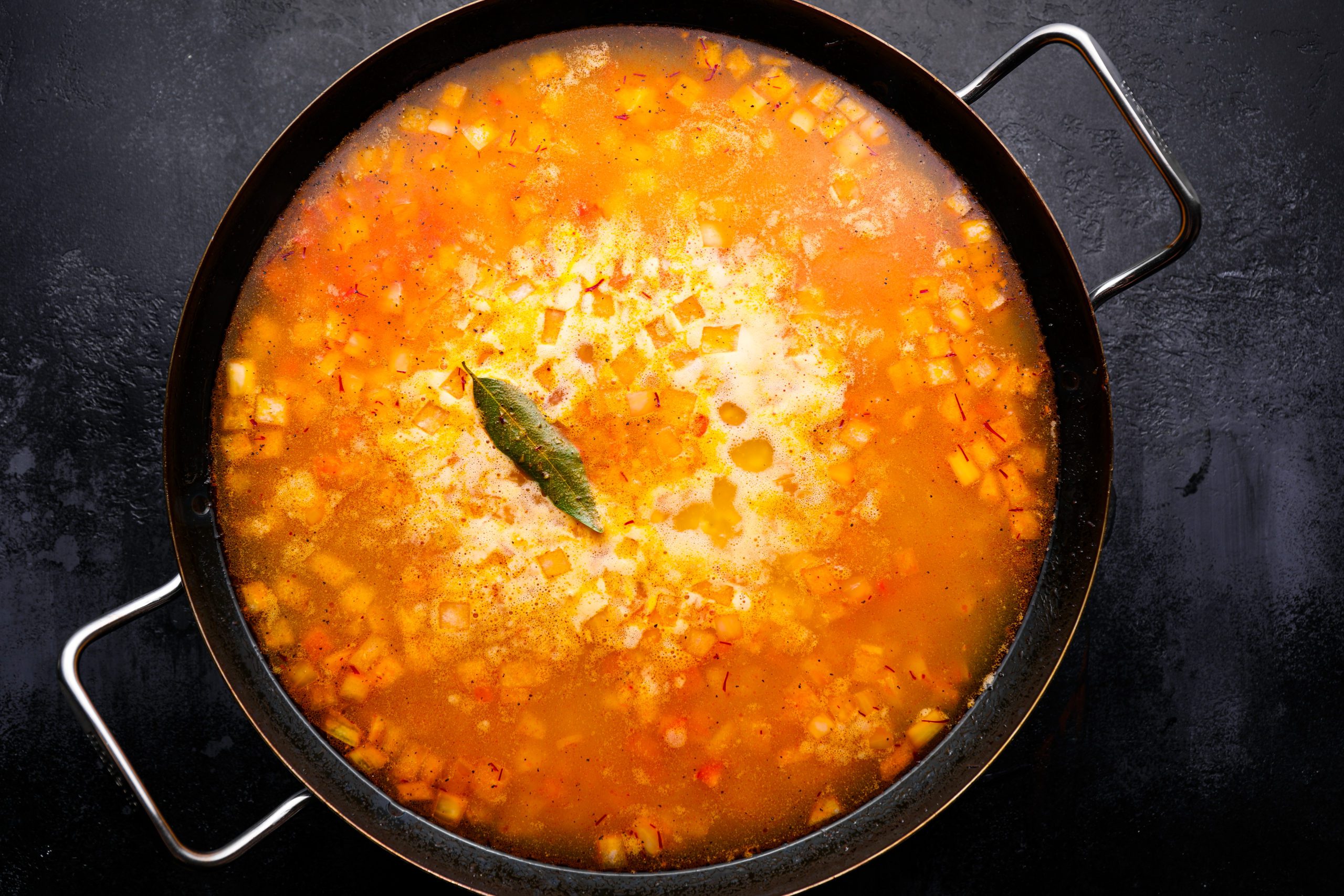 Rice with broth, clam juice, and seasoning in a skillet.