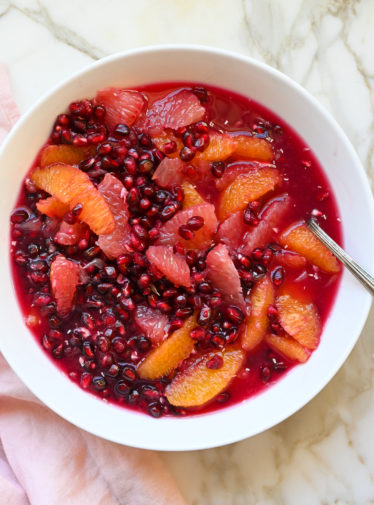 Spoon in a bowl of citrus and pomegranate fruit salad.