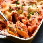 Spoon scooping cheesy stuffed shells from a baking dish.