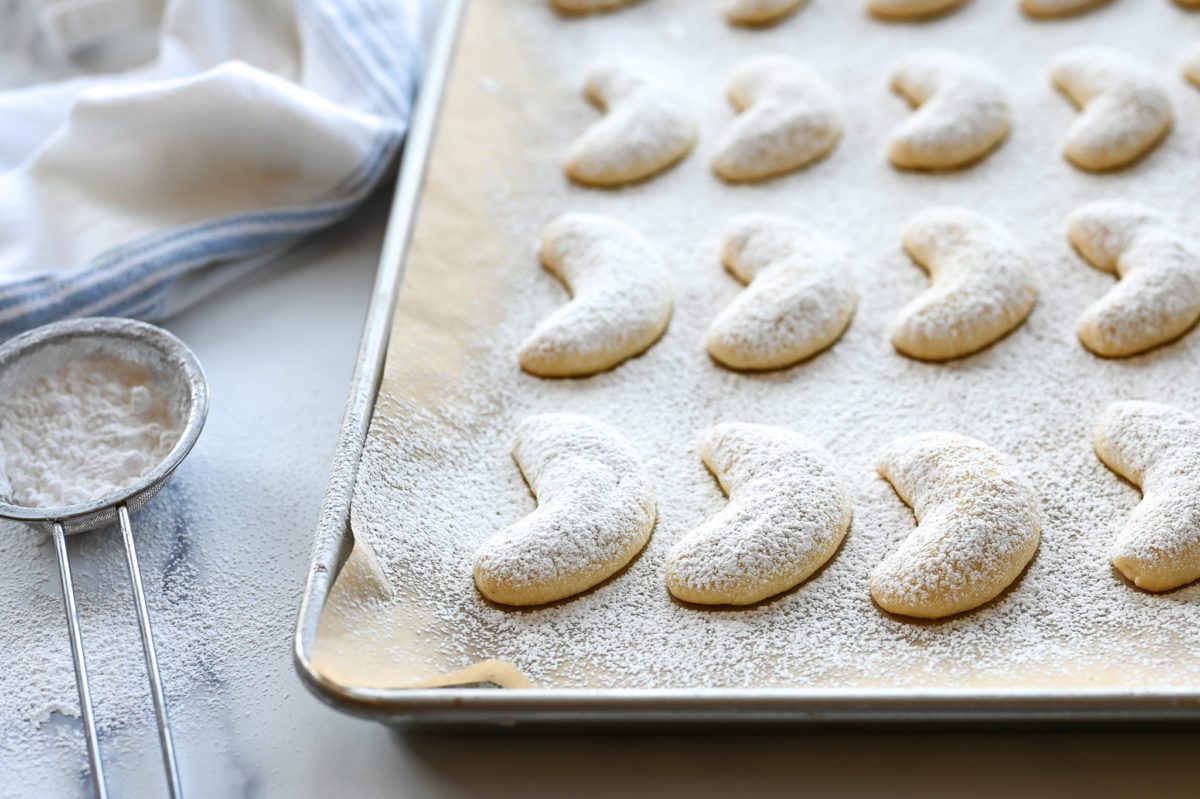 Crescent cookies on a lined baking sheet.