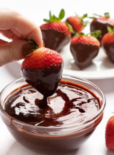 Person dipping a strawberry in chocolate ganache.