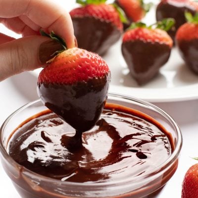 Person dipping a strawberry in chocolate ganache.