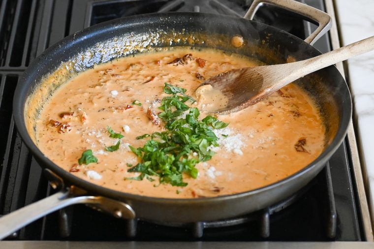 adding basil and cheese to sauce