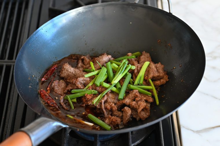 adding the beef and green scallions to the wok
