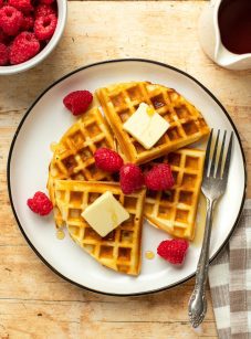 Plate of waffles topped with butter, syrup, and raspberries.