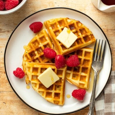 Plate of waffles topped with butter, syrup, and raspberries.