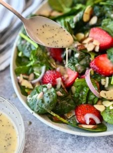Spoon drizzling poppy seed dressing onto a salad.