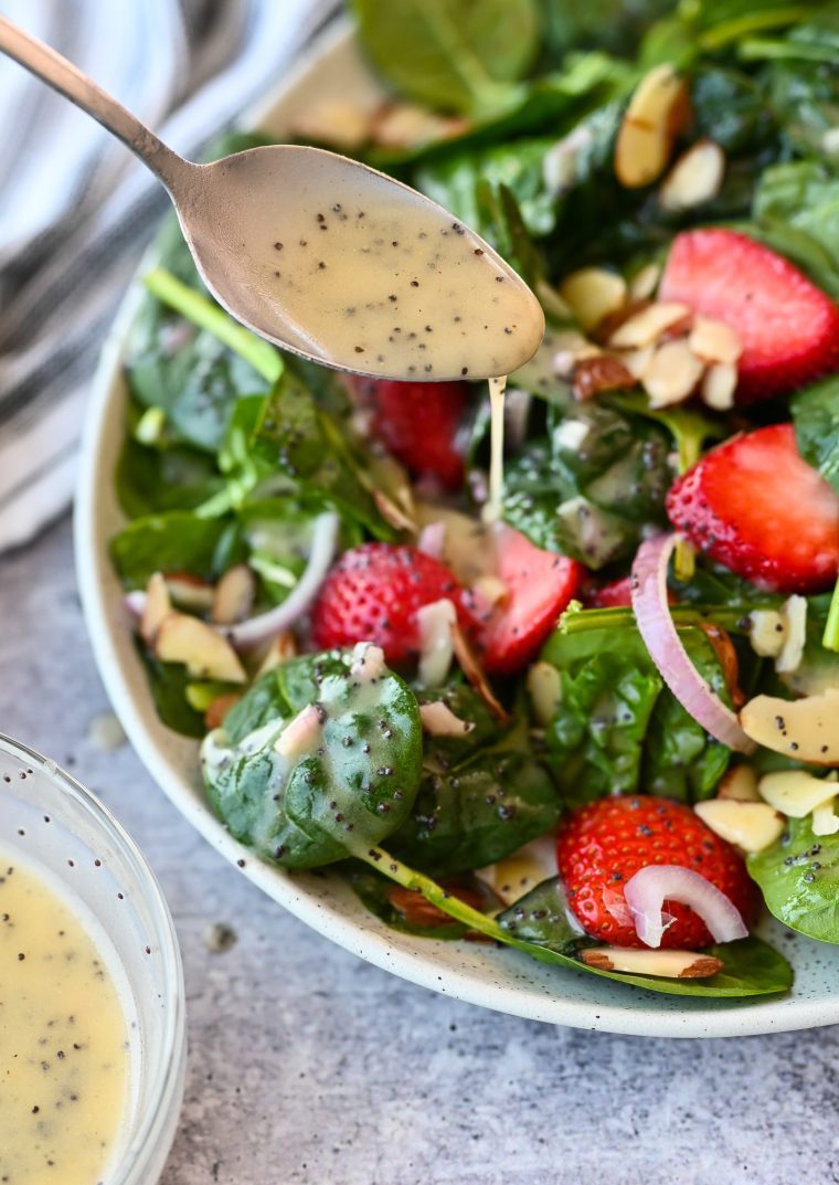 Spoon drizzling poppy seed dressing onto a salad.