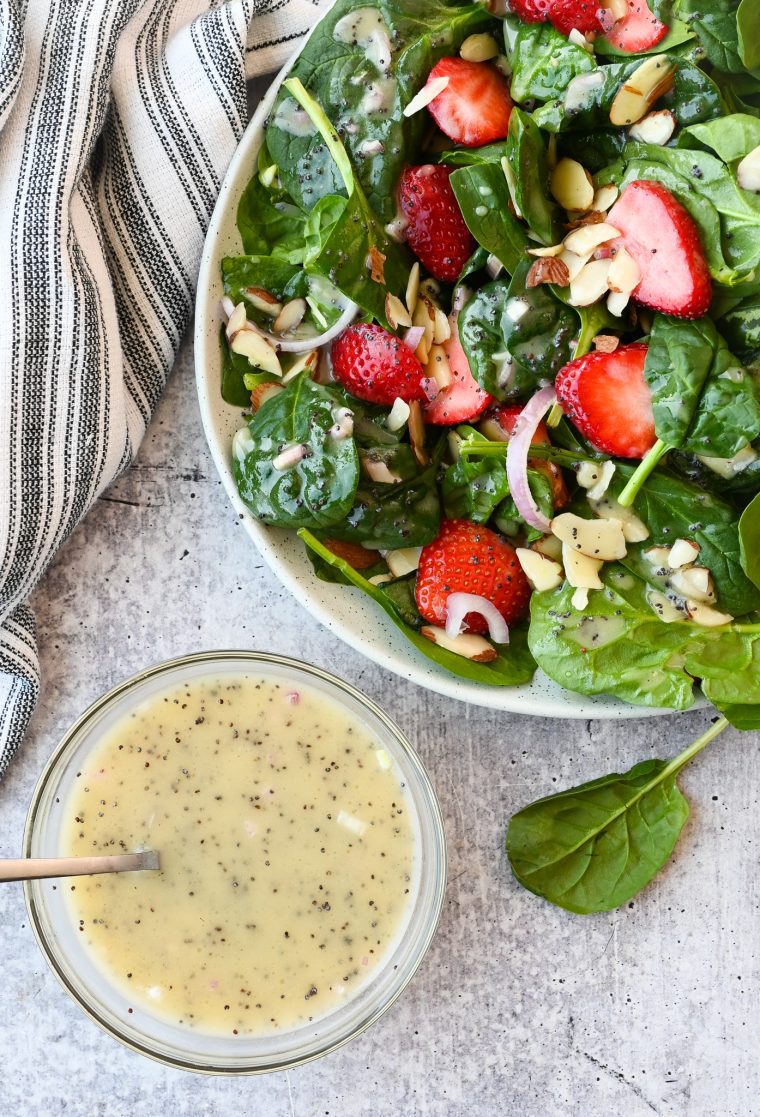 Bowl of poppy seed dressing next to a salad.