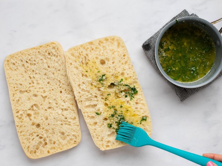spooning the garlic butter mixture over the cut sides of the bread