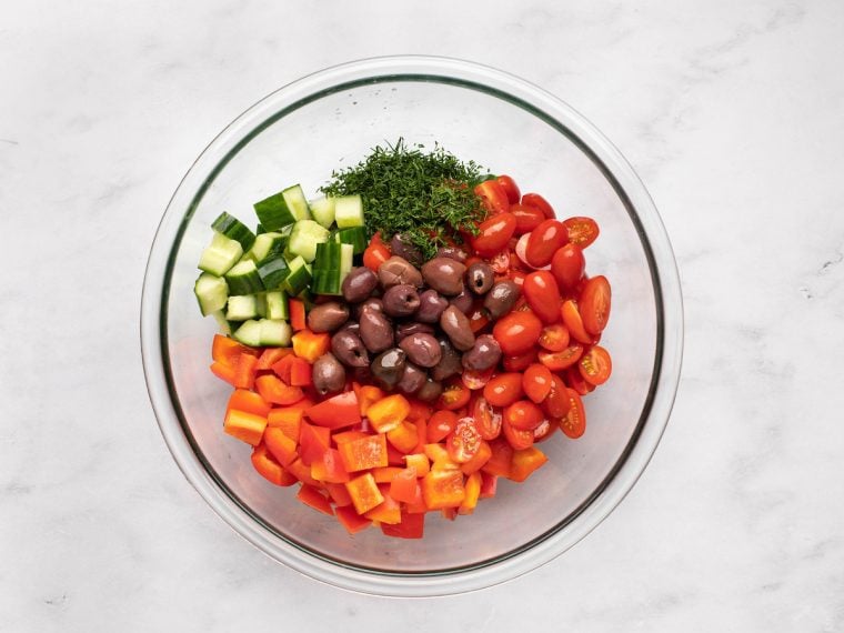 cucumber, peppers, tomatoes, olives, and dill added to bowl with dressing