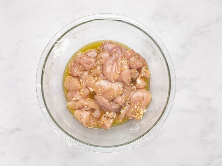 chicken coated in marinade in the bowl covered with plastic wrap