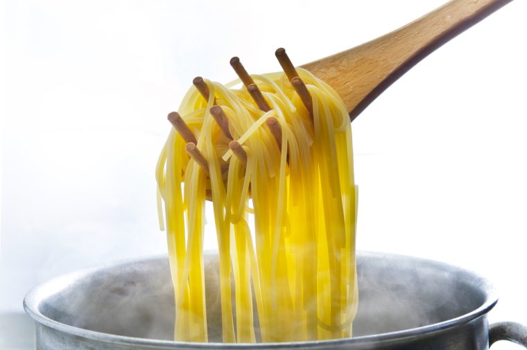 Wooden pasta scoop with steaming noodles.