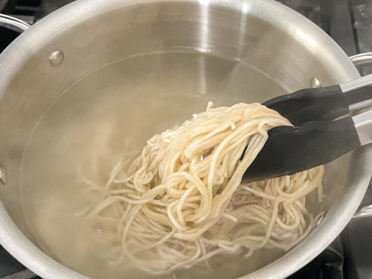 Tongs grabbing cooked noodles from a pot.