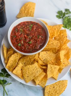 Bowl of salsa on a plate with chips.