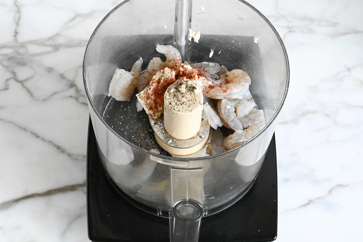 Third of shrimp in food processor with seasoning.