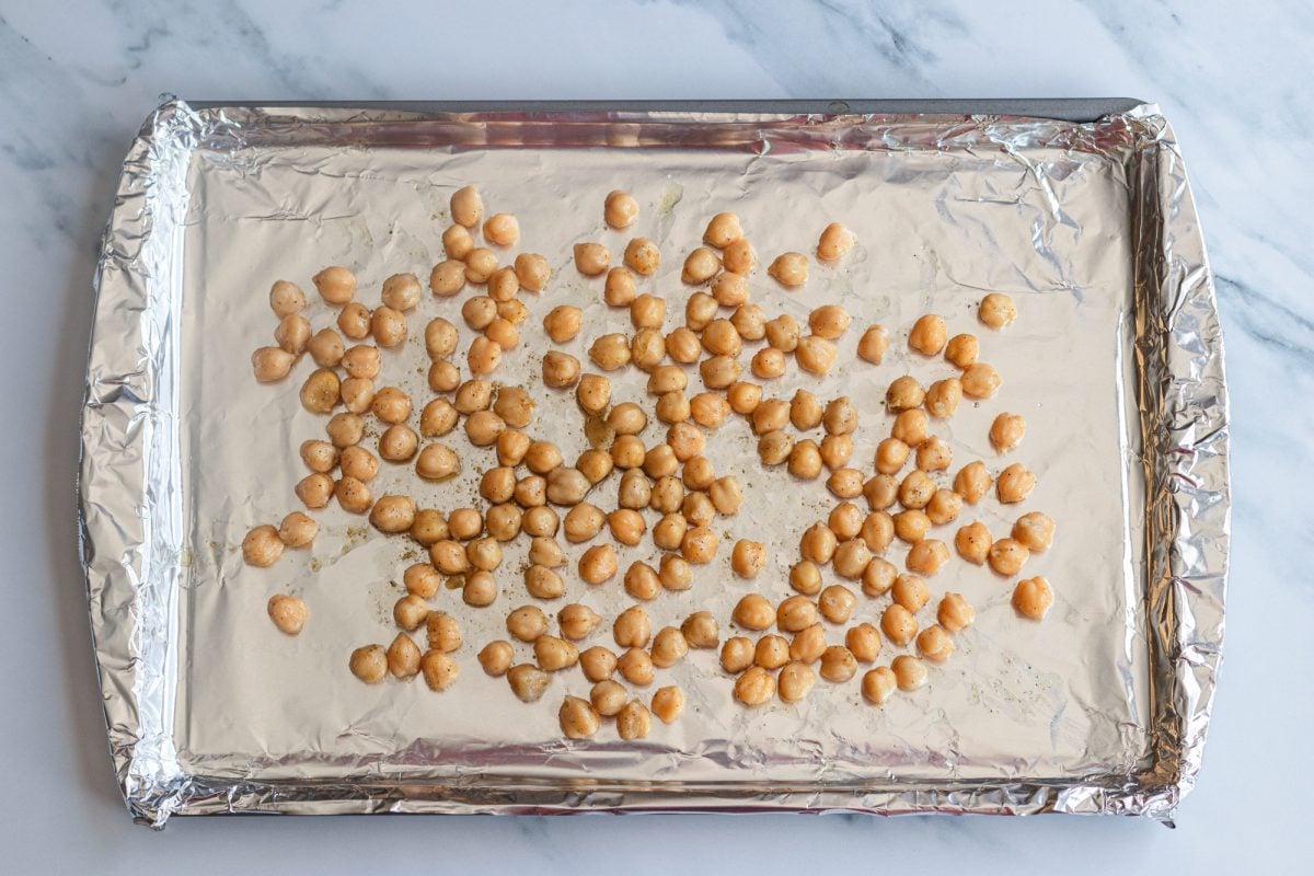 Uncooked chickpeas on baking sheet tossed with olive oil, salt, and pepper.