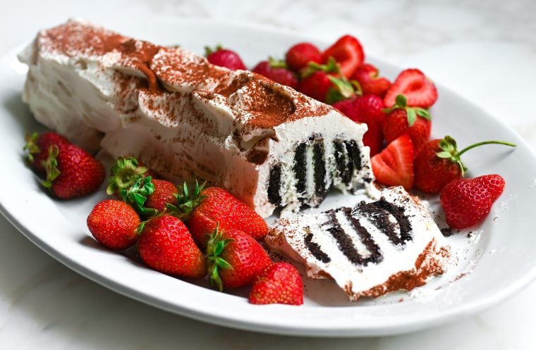 Classic icebox cake with the end cut off, on a plate with strawberries.