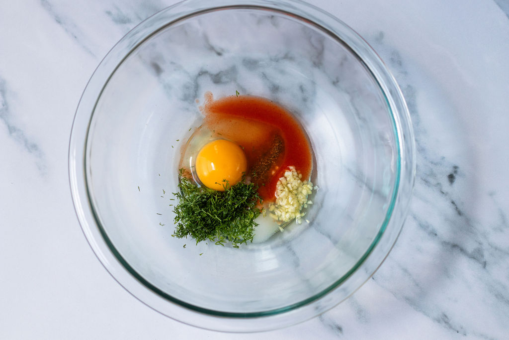 Egg, hot sauce, dill, and garlic in a glass bowl.