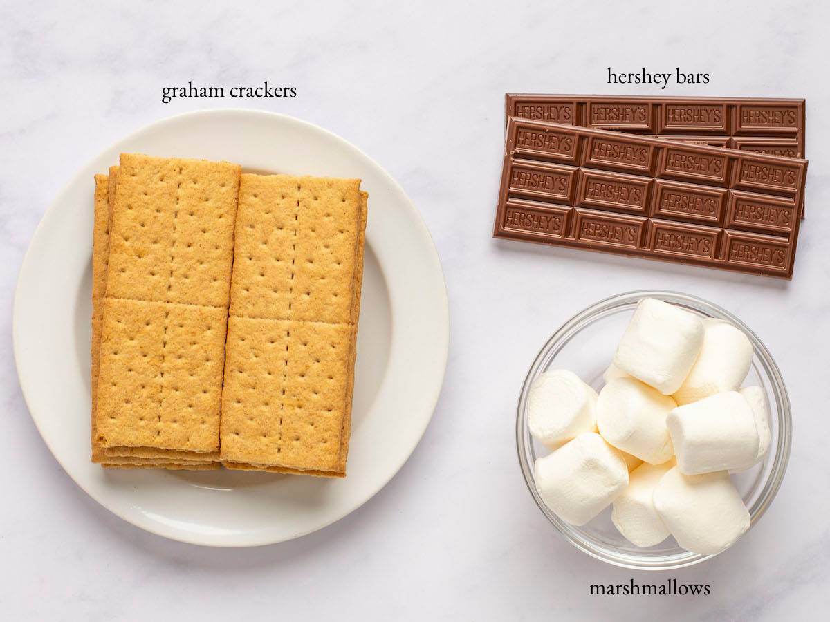 S\'mores ingredients - graham crackers, Hershey bars, and marshmallows - on a marbled surface.