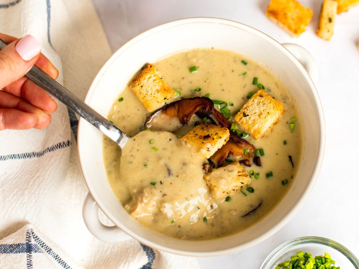 Spoon in a bowl of cream of mushroom soup topped with croutons.